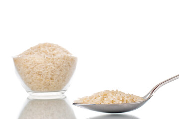 Uncooked organic rice with metal spoon and glassware, macro, isolated on white background.