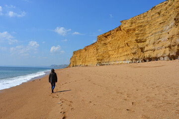 Woman from behind, walking alone beneath the cliffs on Hive Beach, Burton Bradstock, Dorset, England