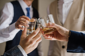 Groom with bestmen drinks whiskey from glasses. Closeup