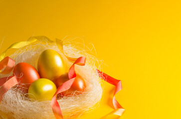 Easter colored eggs of yellow and red color in a nest of white sisal. On a yellow background.