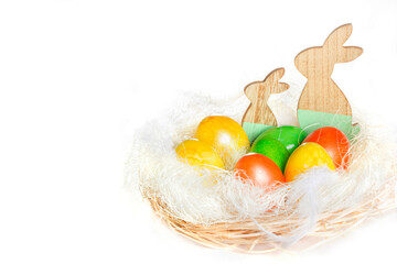 Сomposition for easter in a wicker basket colorful eggs and wooden bunnys on white background. Copy space.