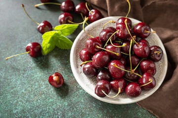 Fresh ripe organic berry red sweet cherries on plate on a dark stone tabletop. Copy space.
