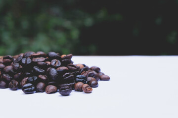 Roasted coffee beans on white table with green leaf background 