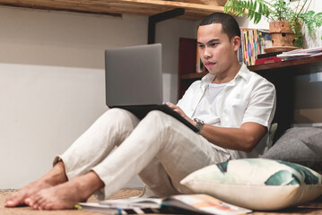 Asian man sit with knees up to use laptop in living room.
