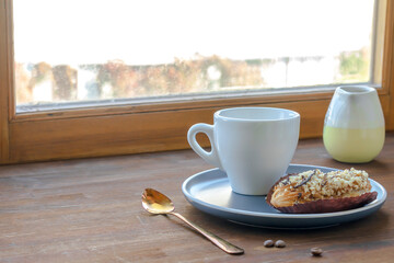 white espresso coffee cup, fresh baked eclair sweet dessert on plate kitchen table against window, utensils dishware, milk jug, home green plant. morning french home breakfast, copy space