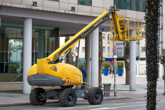 articulated boom lift of yellow color parked on the street with the empty basket