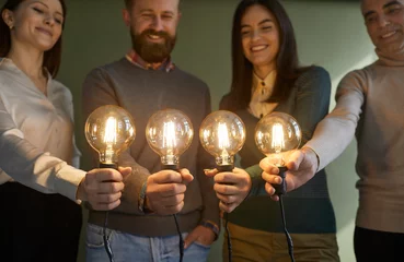 Foto op Plexiglas Happy creative business team developing innovative ideas together. Group of four clever people holding bright, shining, glowing Edison light bulbs. Close up, closeup shot. Idea and innovation concept © Studio Romantic