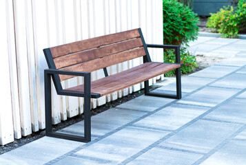 modern bench on the street on a summer day against the backdrop of green bushes. wooden bench in...