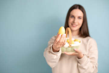 Cute brunette woman holds painted Easter eggs in basket in her hands, Easter, in the studio on a blue background.