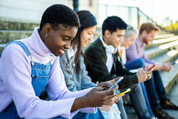 Smiling young people looking at cellphone in city street - Group of multiracial friends relaxing outdoors using mobile phone - Technology and social media concept