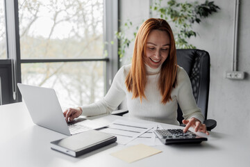 Financial advisor calculating and working in an office. Cheerful mid aged accountant at her desk....
