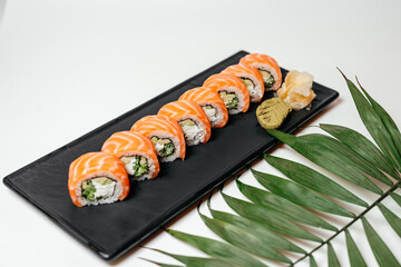 Sushi, rolls, net with palm leaf. Chinese and Japanese cuisine, sets of rolls of ginger and soy sauce lie on a black board with chopsticks. Sushi is made in sets