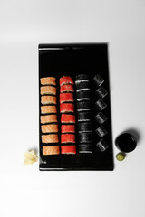 Sushi, rolls. Chinese and Asian cuisine, sets of rolls of ginger and soy sauce lie on a black board with chopsticks. Sushi is made in sets