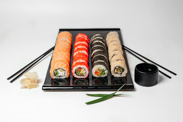 Sushi, rolls. Chinese and Asian cuisine, sets of rolls of ginger and soy sauce lie on a black board with chopsticks. Sushi is made in sets