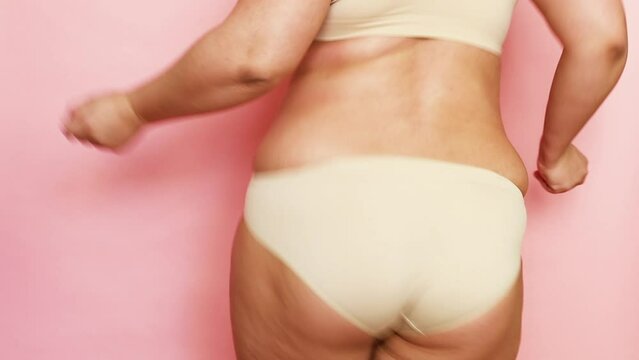 Unrecognizable playful overweight woman with sag hips, buttocks. Dancing and bouncing on pink view. Obesity, excess fat. Cellulite thigh. Fast gain weight. Body positive and acceptance, love yourself