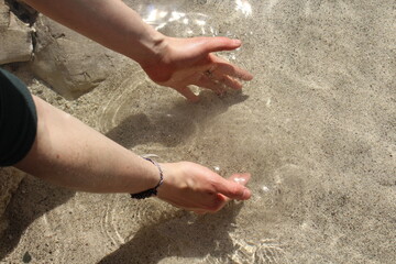 Hands in the water and sand - transparent river. Playing with the water and trying to hold sand