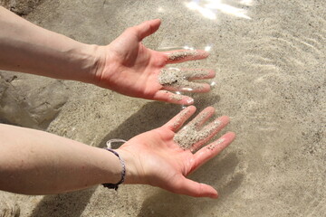 Hands holding sand - water reflection. Close-up of a river with transparent water