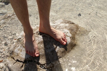 Barefoot on a rock in a river with sand and transparent water