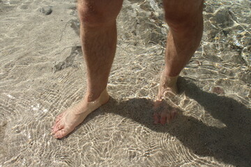 Foot in the water and sand - barefoot in a transparent river. Walking in the water