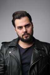 Bearded handsome young man, wearing biker jacket posing on white background.
