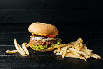composition of hamburger with egg and french fries on a black wooden background