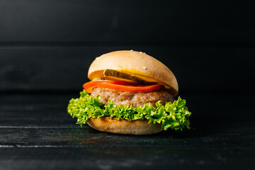 hamburger with tomato and cucumber on a black wooden background