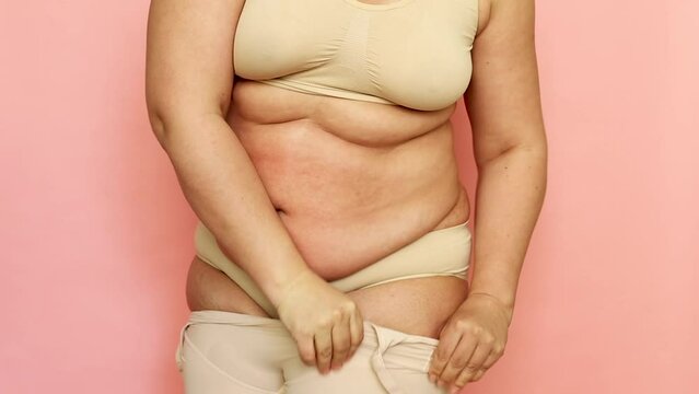 Cropped studio shot of fat overweight woman in special fitness beige shape wear. Fast gain weight with pregnancy. Body health care. Visceral obesity, folds and flabs of dehydrated dozed body. 