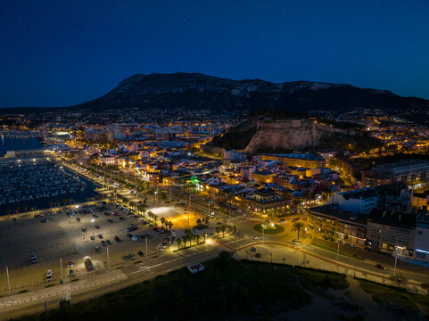 Denia on the Costa Blanca in the evening after the blue hour. A drone shot from the edge of the harbour.