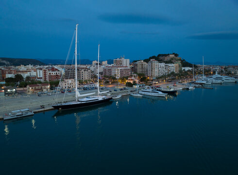 Denia on the Costa Blanca early in the morning at the blue hour. Ships are in port. In the foreground is a large sailing yacht.