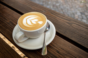 Outdoor Vintage mood, Cappuccino on top with heart flower latte art lay on wooden outdoor bench. Love latte art on coffee cappuccino . Heart and flower latte art pattern.