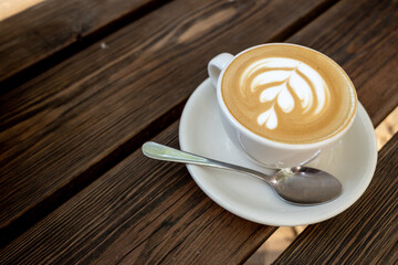 Outdoor Vintage mood, Cappuccino on top with heart flower latte art lay on wooden outdoor bench. Love latte art on coffee cappuccino . Heart and flower latte art pattern.