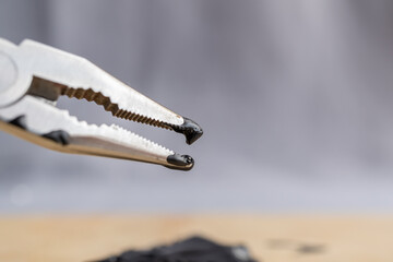 detalle de pinza con las puntas sucias con pintura negra espesa y fondo gris