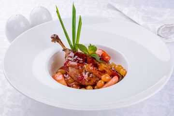 Duck leg confit with flambe fruits and sauce on a white plate