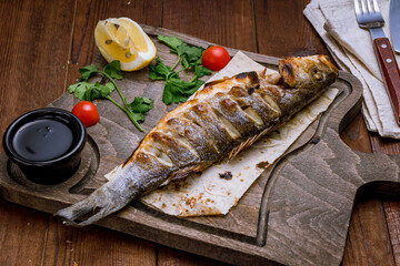 Fried sea bass on grill on a wooden board with lemon on wooden table