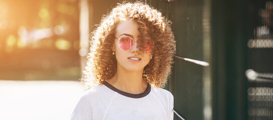 Photo portrait of girl with curly hairstyle wearing white t-shirt and pink glasses outdoor
