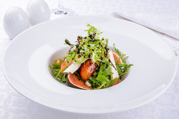 Salad with cheese and figs with flambe fruits and greens on a white plate