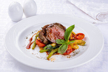 medallions of beef with grilled vegetables on a white plate on white table
