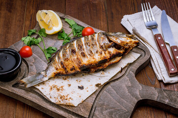 Dorado on grill on a wooden board with lemon on wooden table