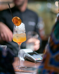 Orange cocktail on the bar counter with a cash register in the background.
