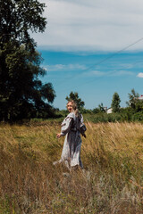  A young woman in a long country dress runs through the field and looks back