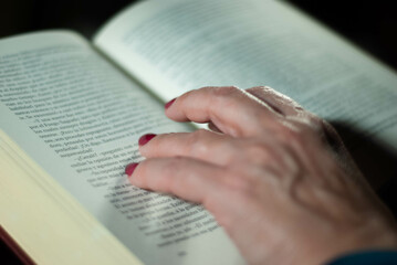 Fototapeta premium Hands holding a book that an elderly woman is reading using her fingers on the lines filled with words