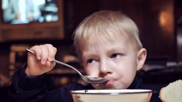 cute child eats soup at the table. boy having lunch. social inequality, poverty