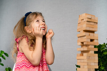 a little happy girl is playing the board game jenga at the table. Construction of a tower made of...