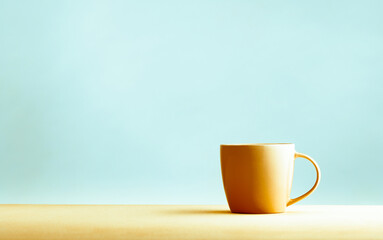 A yellow coffee cup  on yellow table on a blue background. The concept of minimalism. Place for...