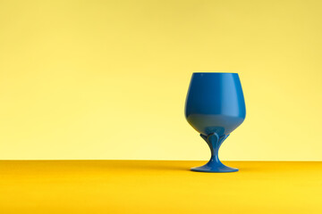Blue wine glass on a yellow table against a yellow background.  Concept of minimalism. Place for...