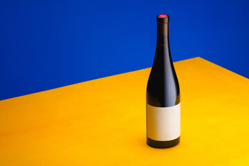 Bottle of wine on a yellow table on a blue background. The concept of minimalism. Poster for...