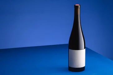 Rolgordijnen Bottle of wine on a blue table on a blue background. The concept of minimalism. Poster for advertising. Place for text  © Vitte Yevhen
