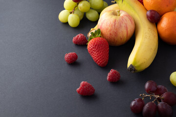 fruit still life on a greyish black background strawberries, apples, bananas, grapes, tangerines with negative space or air for text