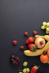 fruit still life on a greyish black background strawberries, apples, bananas, grapes, tangerines with negative space or air for text