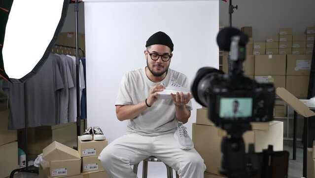 Young attractive Asian man blogger or vlogger looking at camera reviewing product and merchandise. Business online influencer on social media concept.